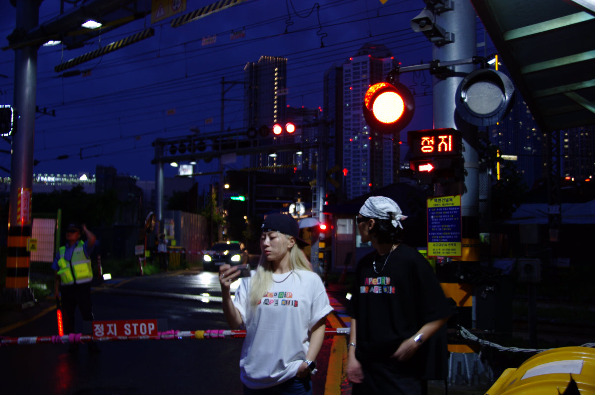 Two people walking on a street at night with traffic lights and buildings in the background.